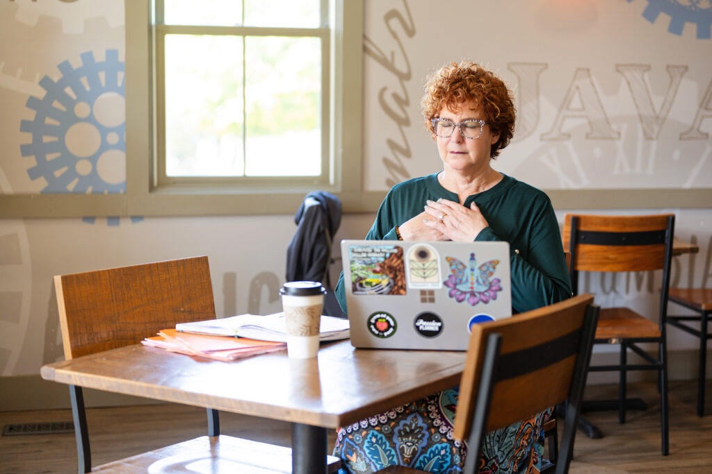 A photo of Allison Field collecting her thoughts with both hands over heart heart in front of an open laptop